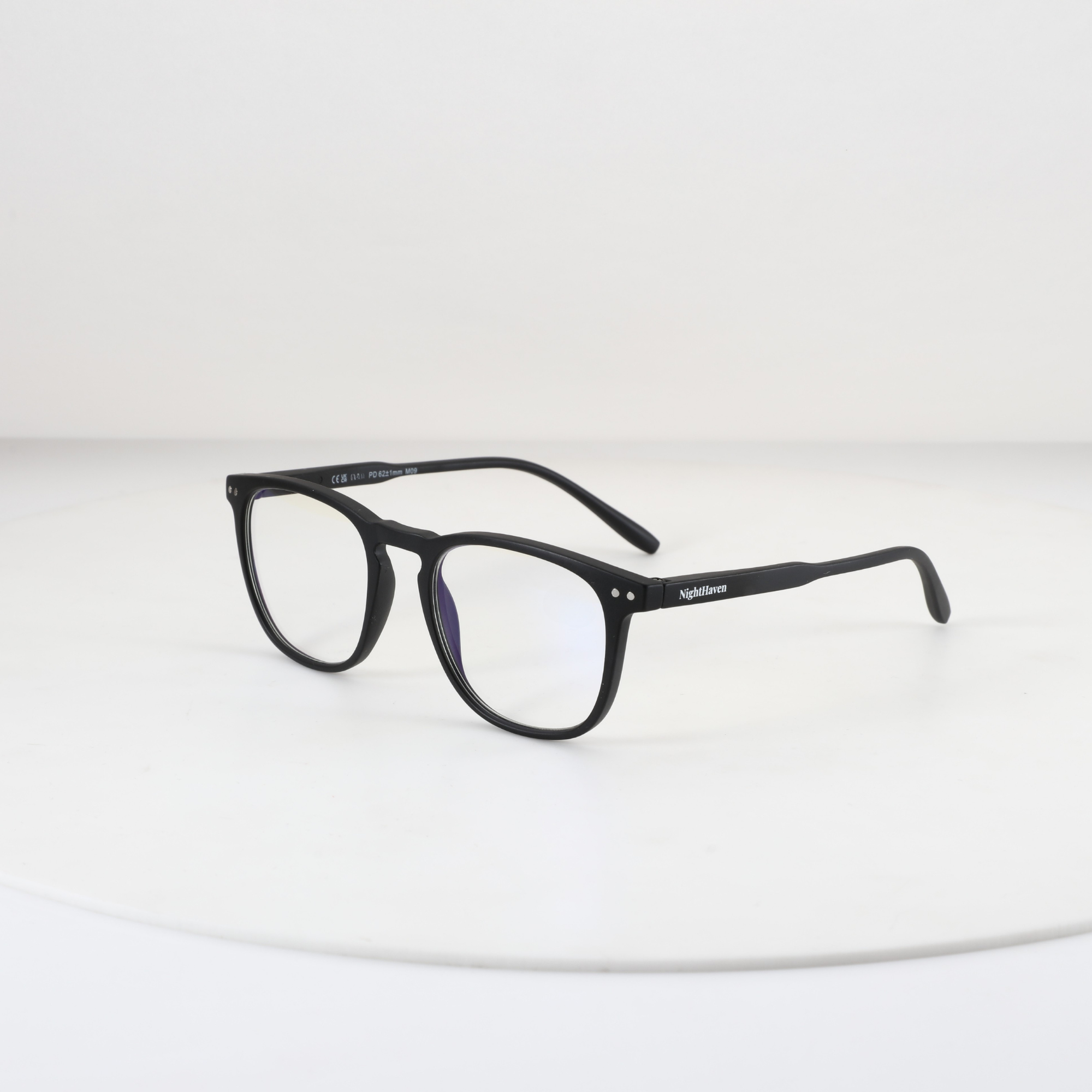NightHaven Blaulichtfilterbrille VESPER™ Crystal Clear – Schrägansicht mit mattschwarzem Wayfarer-Gestell und klaren Blaulichtfilter-Gläsern auf weissem Podest