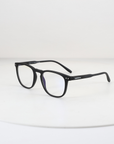 NightHaven Blaulichtfilterbrille VESPER™ Crystal Clear – Schrägansicht mit mattschwarzem Wayfarer-Gestell und klaren Blaulichtfilter-Gläsern auf weissem Podest